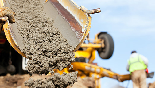 A construction worker is guiding a cement mixer truck chute as concrete is being offloaded for a new house footing. The background is overcast blue sky with another worker, wearing a safety vest, cleaning a mixer chute. http://www.banksphotos.com/LightboxBanners/Concrete.jpg